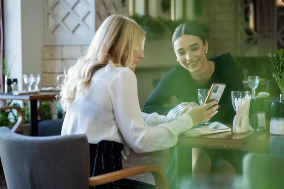 Dos amigas en una mesa del restaurante, con el celular en la mano